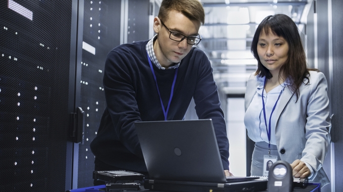 Workers examine a laptop in a server room.